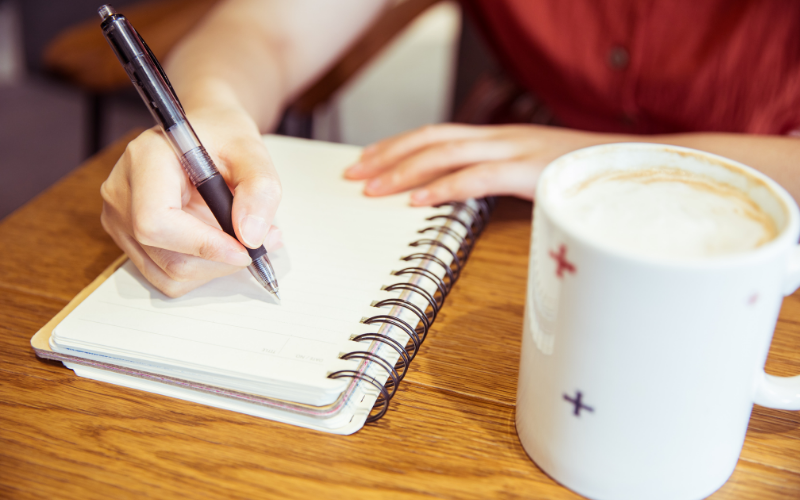 Schreibende Hand mit Kaffee daneben
